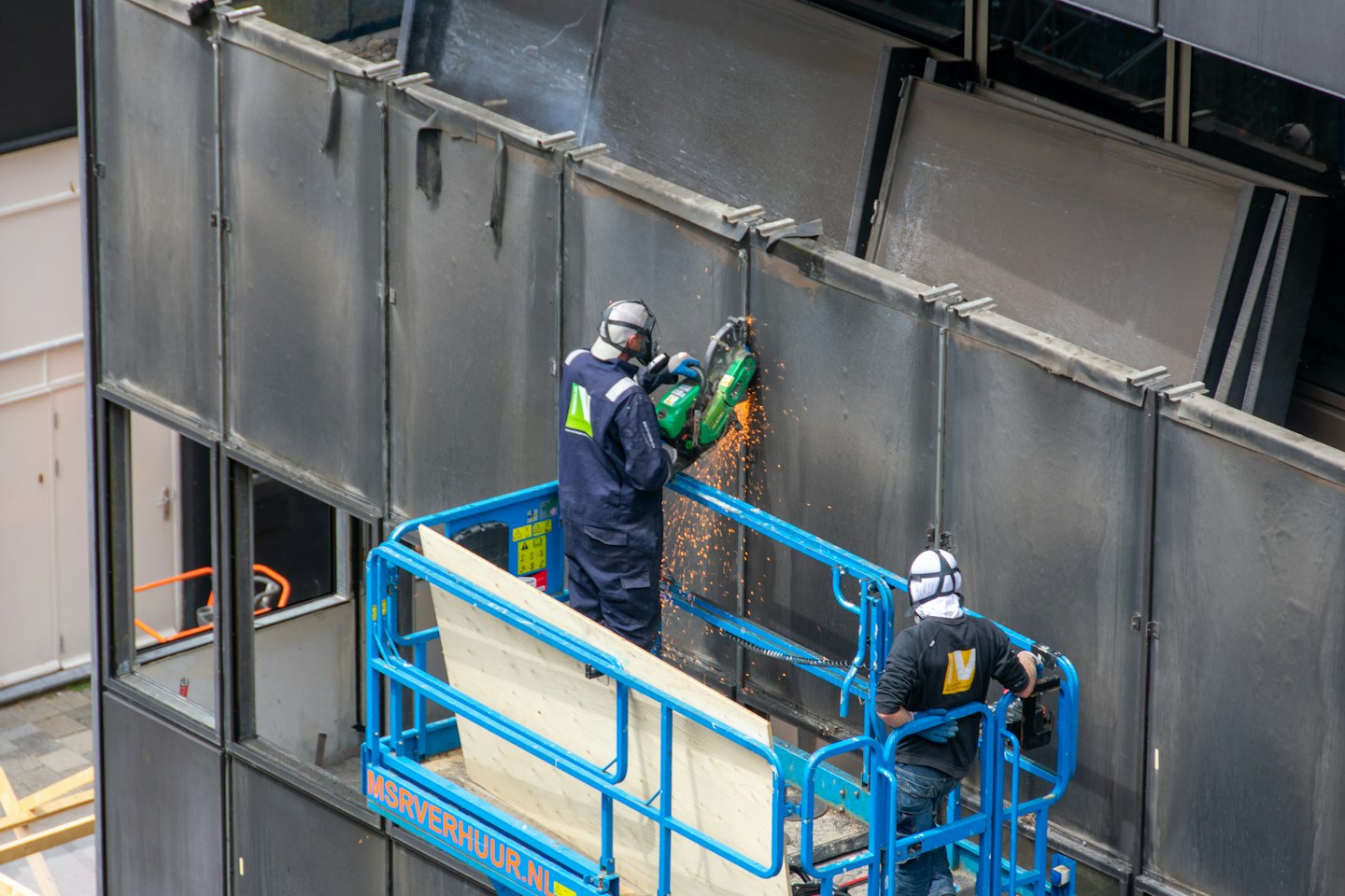 Construction workers in safety gear use a cut-off saw on metal.