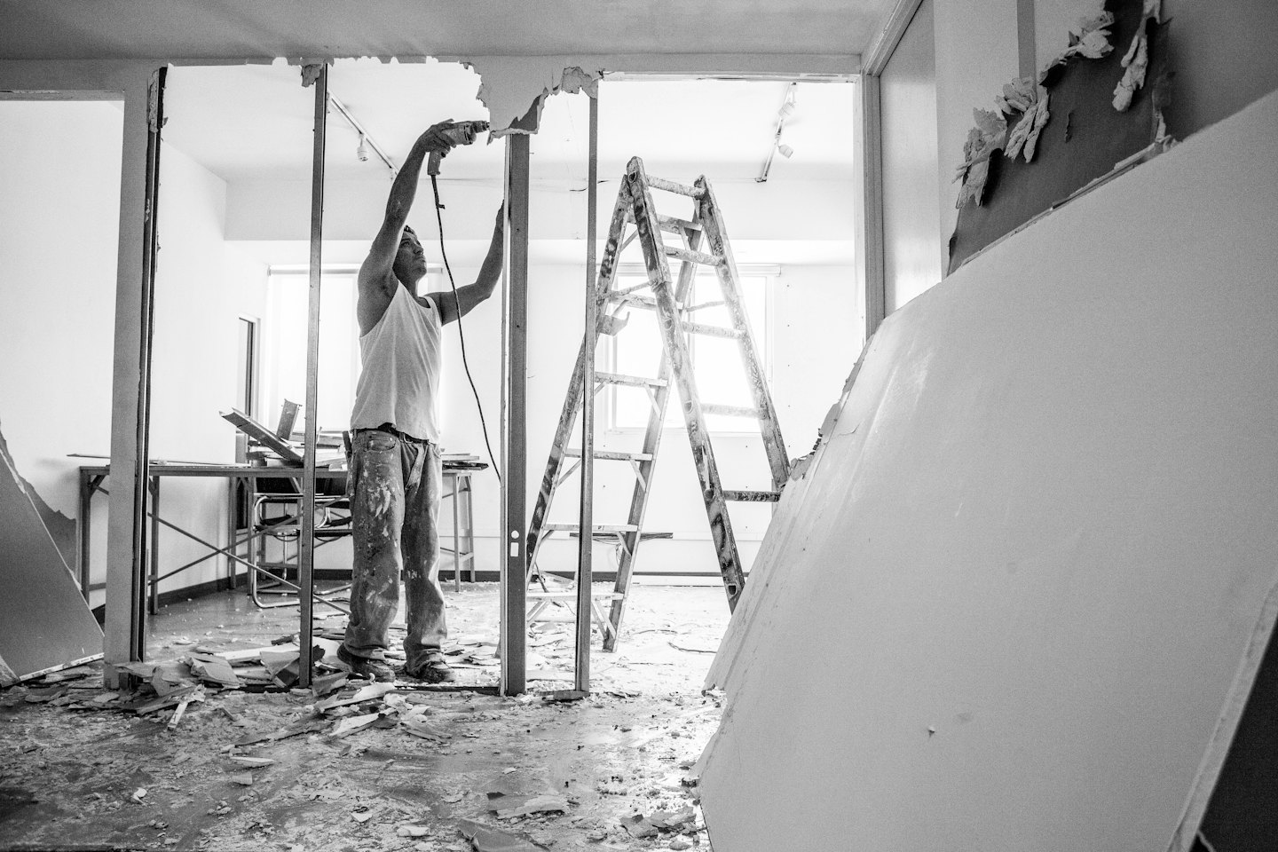 Construction worker demolishes interior wall with power tool.