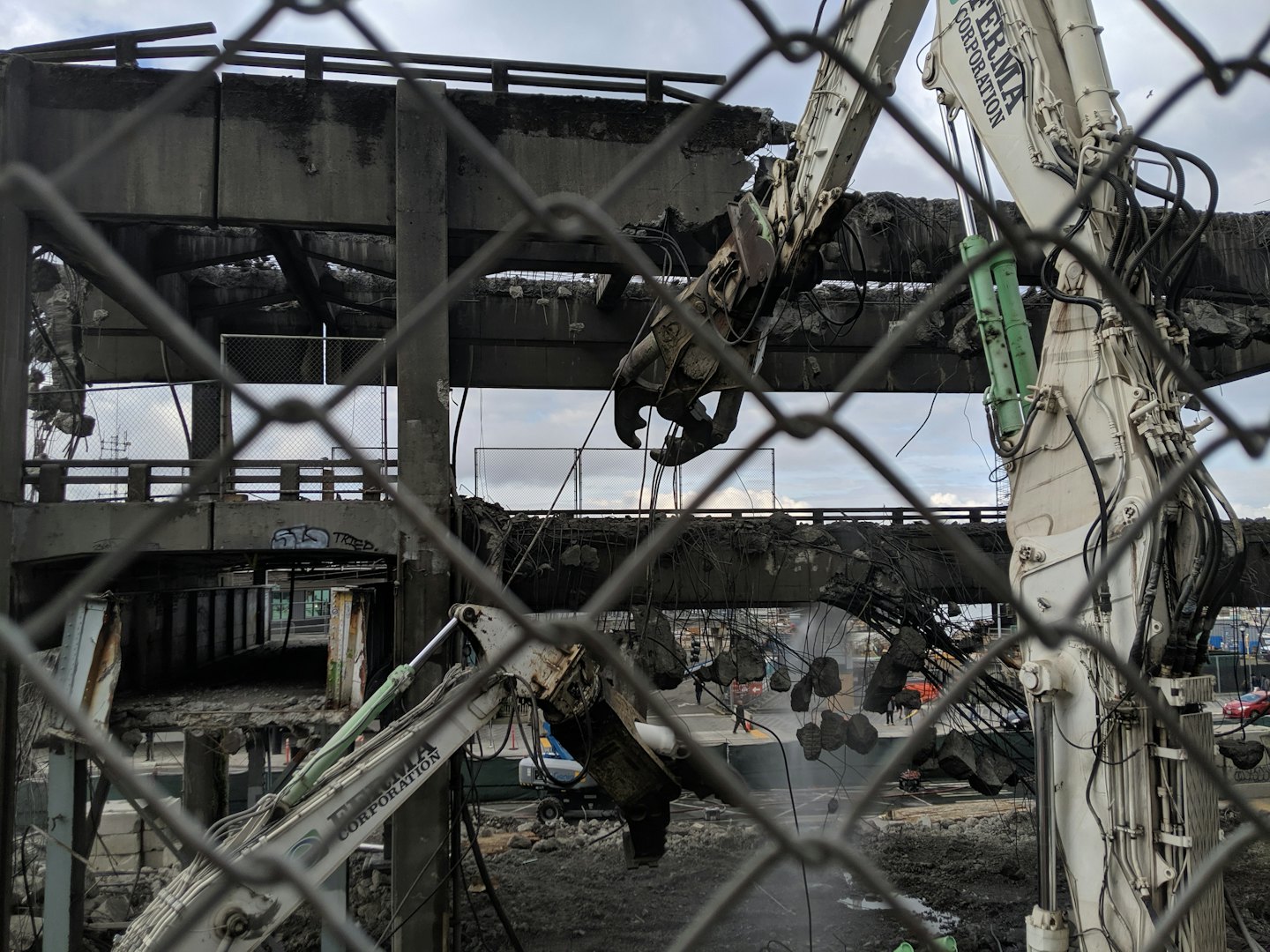 Two excavators dismantle a large concrete structure at a demolition site.